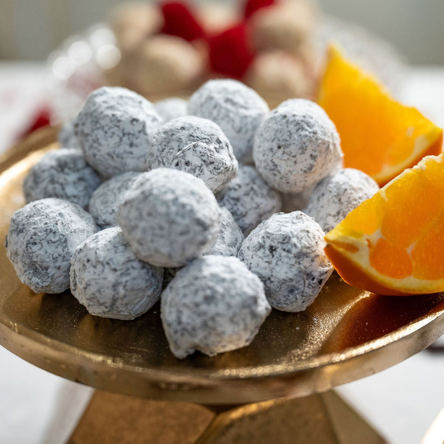 A plate of dark chocolate orange truffles dusted with powdered sugar, accompanied by a slice of orange.