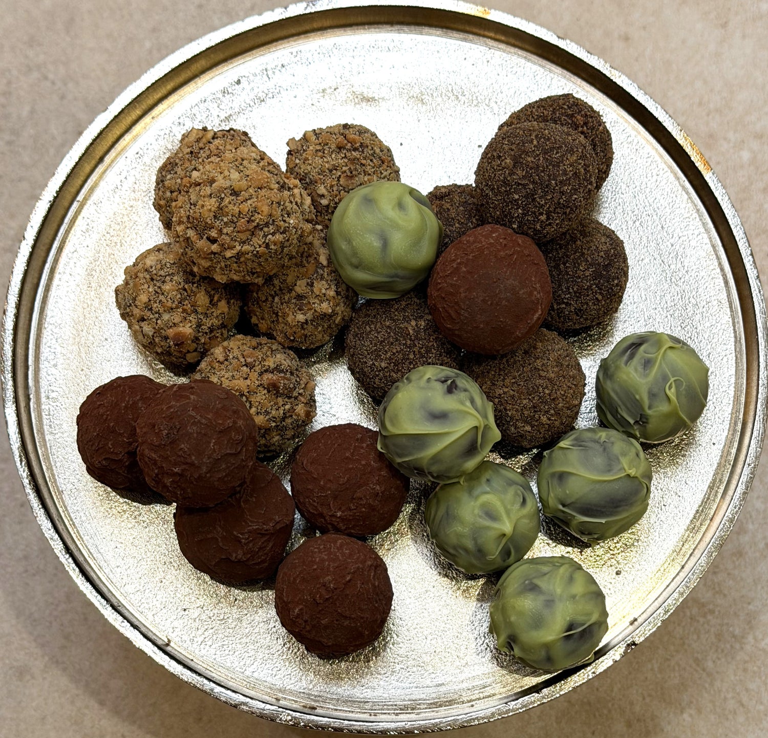 Assorted truffles including brown and green varieties on a metallic surface.